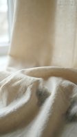Soft beige linen fabric with natural wrinkles and folds in warm morning sunlight creating cozy textile background for home decor and fashion projects.