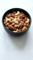 Mixed nuts with sea salt in black ceramic bowl on marble surface for healthy snacking and cooking recipes.