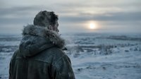 Person wearing hooded winter jacket standing in snowy landscape at sunset, rear view, cold weather outdoor scene.