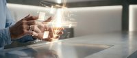 Young adult male with medium skin tone wearing casual blue shirt, hands positioned over desk surface interacting with glowing digital interface and holographic data visualization for business, technology, and innovation concepts.