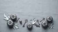 Autumn flat lay with metallic silver pumpkins, vintage keys and oak leaves arranged on textured gray background for seasonal home decor projects.