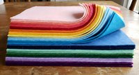 Colorful felt fabric sheets stack in rainbow arrangement on wooden table for crafting sewing quilting and DIY projects creative materials supply.