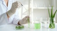Scientist in white lab coat using pipette to extract green plant essence in modern laboratory with glassware and botanical samples for research and development.