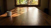 Wooden desk with white mug bathed in warm sunlight streaming through window, creating natural shadows and golden light for workspace and office design projects.