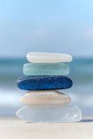 Stacked sea glass stones in white, aqua, blue and tan tones balanced on sandy beach with ocean backdrop. Wellness and relaxation concept.