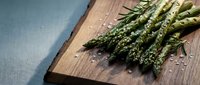 Fresh green asparagus spears with rosemary and sea salt on wooden cutting board, ready for healthy cooking and gourmet meal preparation.