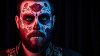 Man with Day of the Dead sugar skull face paint in red and blue lighting. Halloween makeup design for costume party and cultural celebration.