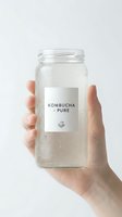 Hand holding glass jar of fermented kombucha tea with minimalist label on clean white background for health and wellness branding.