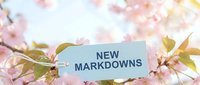 New markdowns tag among blooming pink cherry blossom branches in soft spring light, perfect for seasonal sale promotions and retail marketing.