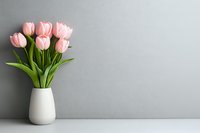 Fresh pink tulips in white ceramic vase against gray wall background on white surface, minimalist spring floral arrangement with copy space.