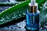 Blue serum bottle with silver dropper cap against wet green aloe vera leaf background, water drops on dark surface for cosmetic and skincare advertising.