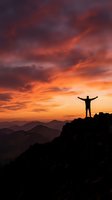 Silhouette of triumphant man with raised arms standing on mountain peak against dramatic orange and purple sunset sky with layered mountain ranges.