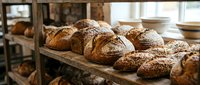 Freshly baked artisan bread loaves with crispy crust dusted with flour arranged on wooden shelf in rustic bakery setting for food and culinary use.