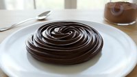 Rich dark chocolate ganache swirl on white plate, perfect for dessert presentation, baking projects, culinary arts, and gourmet food photography applications.