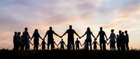 Large group of diverse people holding hands in silhouette against dramatic sunset sky, symbolizing unity, teamwork and community connection for business concepts.