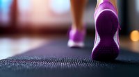 Close-up view of purple athletic shoes walking on textured black exercise mat, showing motion and fitness activity in soft focus background.