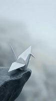 White origami paper crane perched on stone ledge against misty cloudy sky background symbolizing peace hope freedom and mindfulness meditation concepts.