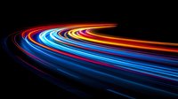 Vibrant light trails curve along dark background creating dynamic motion effect with red, blue and yellow streaks, long exposure photography technique for abstract backgrounds.