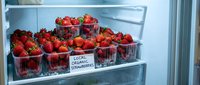 Fresh organic strawberries in plastic containers stored in refrigerator with local farmers market label for healthy eating and food storage.