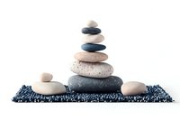 Balanced zen stones pyramid on blue textured mat against white background, creating peaceful spa and meditation atmosphere for wellness concepts.
