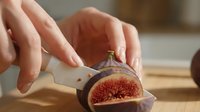 Fresh fig cut in half showing red interior flesh and seeds, held in hand on wooden surface for food styling and culinary use.