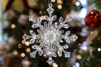 Crystal snowflake ornament with intricate details hanging against blurred holiday lights background, creating magical winter atmosphere for festive decorations.