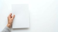 Close-up of hand holding blank white paper sheet against neutral background, suitable for mockups, presentations, and design templates.