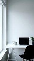 Clean minimalist home office workspace with laptop computer and coffee mug on white desk by window with natural light and modern black chair.