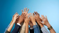 Diverse group of hands raised up against blue sky background showing unity, teamwork and collaboration in business or community setting.
