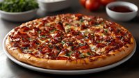 Fresh baked BBQ chicken pizza with melted cheese, crispy bacon bits, red onions and chopped herbs on round white plate against dark background.
