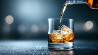 Pouring golden whiskey into glass with ice cubes on dark background with bokeh lights, dynamic splash motion capture for beverage advertising.
