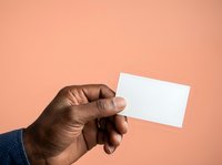 Man with dark skin tone holding blank white business card against peachy background for corporate branding and professional networking purposes.