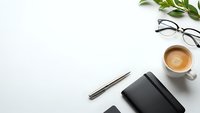 Minimalist workspace with coffee cup, notebook, pen and glasses on white desk. Clean office setup for productivity and business planning.