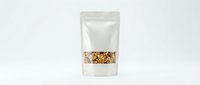 White stand-up pouch with transparent window showing granola or mixed nuts inside, placed on light background for packaging design mockup.