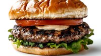 Juicy grilled beef burger with fresh lettuce, tomato slices, and creamy sauce on golden brioche bun, photographed in close-up on white background.