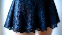 Delicate black lace trim detail on dark blue fabric creates elegant scalloped hem pattern with intricate floral motifs, showcasing fine textile craftsmanship and design.