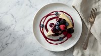 Gourmet dessert pancake topped with fresh berries and berry sauce on marble surface for restaurant menu and food photography.