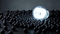 Glowing light bulb surrounded by dark spheres on black surface, symbolizing innovation, unique ideas, and standing out from the crowd for business concepts.