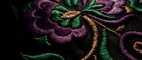 Intricate floral embroidery with purple and green thread on dark fabric showcasing detailed needlework and textile artistry for fashion and craft projects.