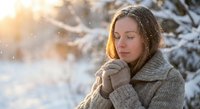 Young woman in cozy sweater enjoying peaceful winter morning with warm sunlight and falling snow in snowy forest landscape for wellness and mindfulness concepts.