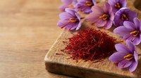 Saffron threads on wooden spoon with purple crocus flowers on rustic wood background. Premium spice for culinary cooking and natural ingredients.