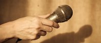 Hand holding professional microphone against warm textured background for broadcasting, podcasting, interviews, music recording and live performance applications.