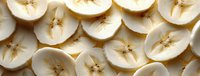 Fresh sliced bananas arranged in rows showing cross sections with white flesh and brown seeds, natural food pattern background for healthy eating concept.