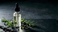 Essential oil bottle with fresh rosemary herbs on dark stone surface for aromatherapy wellness spa treatment and natural skincare products.