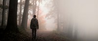 Man walking alone through misty forest path surrounded by tall trees on autumn day, solitude and contemplation concept for wellness and mental health themes.