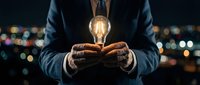 Businessman holding glowing light bulb in hands against city lights background representing innovation, creativity and bright ideas for business success.