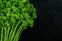 Fresh green curly kale leaves and stems arranged on dark background, organic healthy vegetable produce for nutritious cooking and salads.