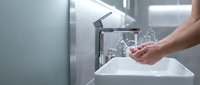 Modern bathroom sink with running water and hands washing in contemporary interior with chrome faucet and clean white basin for hygiene and wellness.