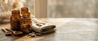 Amber glass jars with wooden spoons and linen cloth on rustic table creating warm natural spa atmosphere for organic skincare and wellness products.