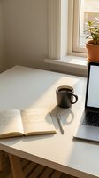 Minimalist workspace with open notebook, black coffee mug, pen, and laptop on white desk by bright window with potted plant, ideal for productivity and remote work concepts.